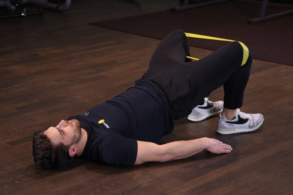 Odwodzenie kolan we wznosie bioder z gumą mini band na kolanach Odwodzenie kolan we wznosie bioder z gumą mini band na kolanach