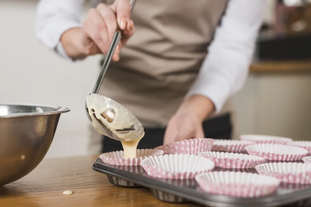 kobieta przelewa ciasto na babeczki do foremek
